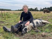Martin Keller sidder på mark og kæler for en gris, der sover i græsset.